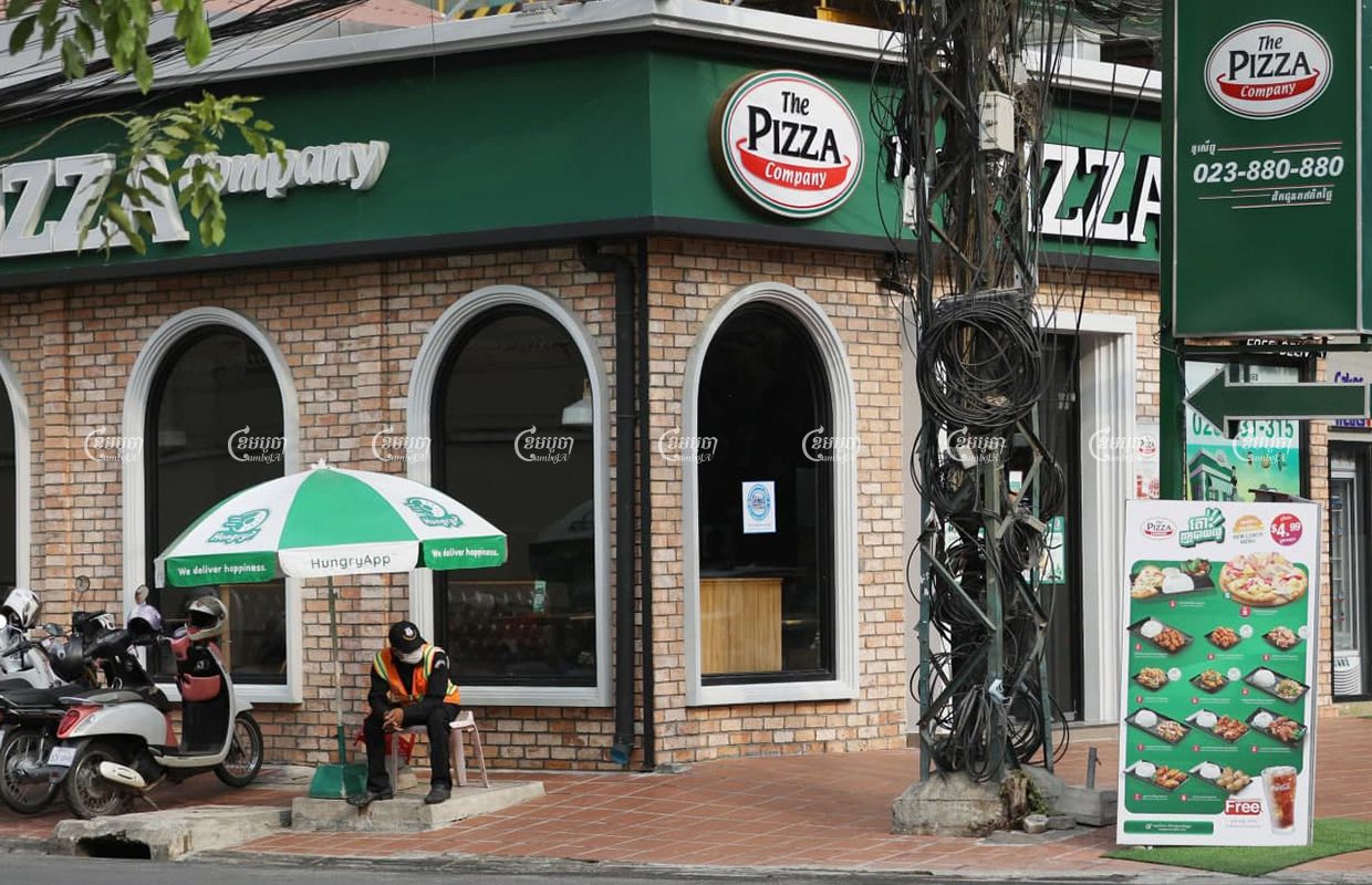 សន្តិសុខម្នាក់អង្គុយនៅមុខហាងភីហ្សាខមផេនី (Pizza Company ) នៅភ្នំពេញថ្ងៃទី ១៨ ខែមីនាឆ្នាំ ២០២១ ។ ខេមបូចា/ព្រីង សំរាំង
