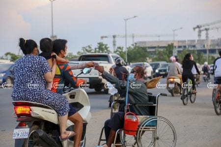 លោកអ៊ុច ភា អង្គុយនៅលើរទេះរុញ ទទួលលុយលក់ទឹកសុទ្ធពីភ្ញៀវ នៅលើផ្លូវ៦០ម៉ែត្រ ក្នុងរាជធានីភ្នំពេញ នៅថ្ងៃទី៩ខែឧសភាឆ្នាំ២០២១។ (ខេមបូចា/ អាន វិចិត្រ)