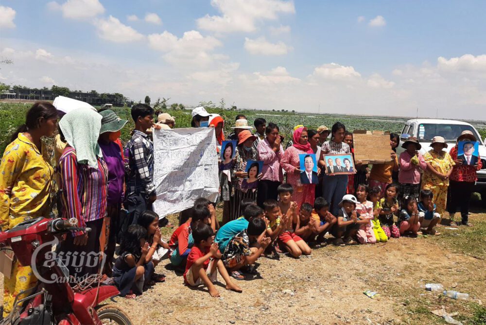 ប្រជាពលរដ្ឋរស់នៅជាប់បឹងតាមោកកំពុងឈរតវ៉ាដោយលើករូបថតថ្នាក់ដឹកនាំ នៅខាងមុខបឹងតាមោកនៅភូមិសំរោងត្បូង សង្កាត់សំរោង ខណ្ឌព្រែកព្នៅ រាជធានីភ្នំពេញ។ រូបថតនៅថ្ងៃទី ២៣ ខែមិថុនា ឆ្នាំ២០២២។ ខេមបូចា/ វ៉ា សុភានុត