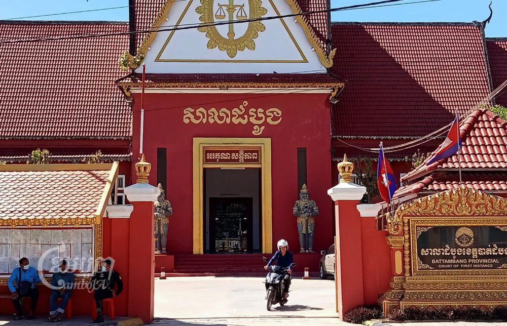 បុរសម្នាក់កំពុងជិះម៉តូចេញពីសាលាដំបូងខេត្តបាត់ដំបង ខណៈបុរសពីរនាក់ផ្សេងទៀតកំពុងជជែកជាមួយមន្ត្រីប៉េអឹមម្នាក់ខាងក្រៅរបងតុលាការខេត្ត។ រូបថតថ្ងៃទី១៦ ខែកញ្ញា ឆ្នាំ២០២២។ ខេមបូចា/ សុខ សាវី