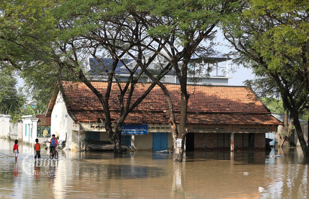 ក្មេងៗដើរឆ្លងទឹក ដែលជន់លិចដោយជំនន់ទឹកភ្លៀង នៅសង្កាត់ព្រែកកំពឹស ជាយក្រុងភ្នំពេញ។ រូបថតថ្ងៃទី១៦ ខែមករា ឆ្នាំ២០២៣។ ខេមបូចា/ ព្រីង សំរាំង