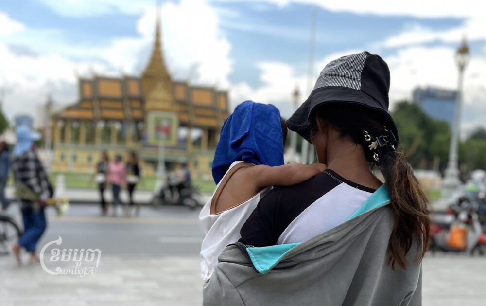 ស្ត្រីម្នាក់ពកូននៅមុខព្រះបរមរាជវាំង រាជធានីភ្នំពេញ។ រូបថតនៅថ្ងៃទី២៨ ខែមិថុនា ឆ្នាំ២០២៣។ ខេមបូចា/ ព្រីង សំរាំង