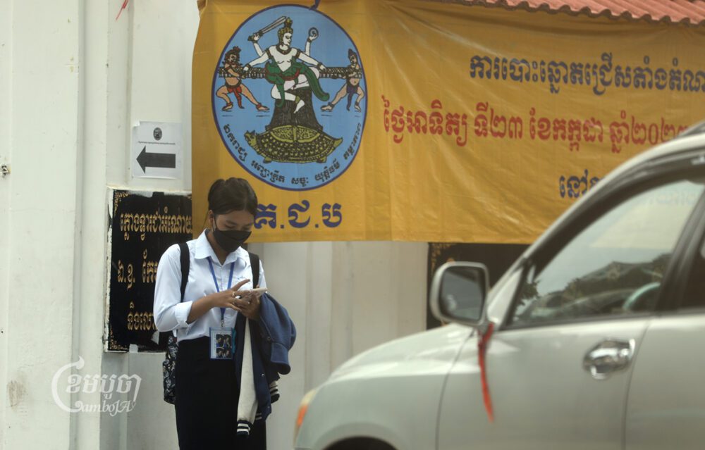 សិស្សម្នាក់កំពុងមើលទូរសព្ទដៃនៅមុខក្លោងទ្វារចូលវិទ្យាល័យបឹងកេងកង រាជធានីភ្នំពេញ កាលពីថ្ងៃទី៧ ខែកក្កដា ឆ្នាំ២០២៣។ (ខេមបូចា/ ព្រីង សំរាំង)