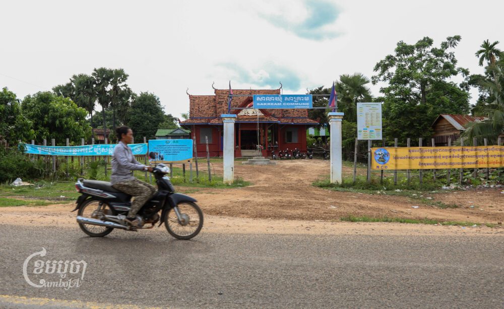 ស្ត្រីម្នាក់កំពុងជិះម៉ូតូកាត់មុខសាលាឃុំសាគ្រាម ស្រុកប្រាសាទបល្ល័ង្ក ខេត្តកំពង់ធំ។ រូបថតនៅថ្ងៃទី២៥ ខែកញ្ញា ឆ្នាំ២០២៣។ (ខេមបូចា/ អាន វិចិត្រ)