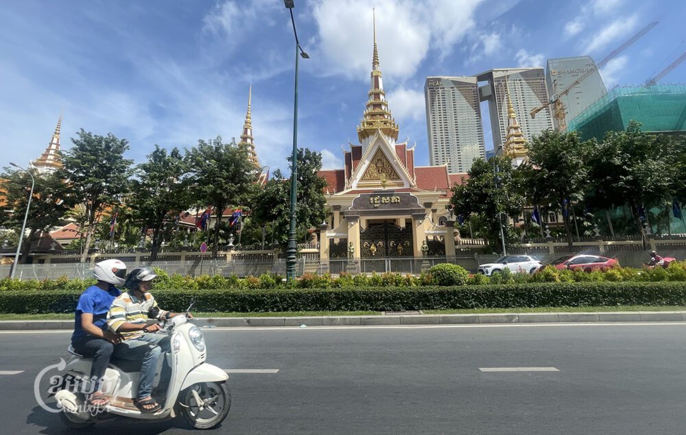 បុរសពីរនាក់បើកម៉ូតូឆ្លងកាត់រដ្ឋសភាក្នុងរាជធានីភ្នំពេញ កាលពីថ្ងៃទី២២ ខែវិច្ឆិកា ឆ្នាំ២០២៣។ (ខេមបូចា/ ព្រីង សំរាំង)