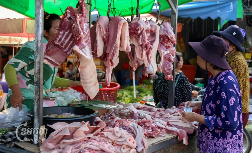 ស្ត្រីចំណាស់ម្នាក់កំពុងឈរកាន់លុយតថ្លៃទិញសាច់ជ្រូកនៅផ្សារមួយក្នុងរាជធានីភ្នំពេញ។ រូបថតថ្ងៃទី២២ ខែកញ្ញា ឆ្នាំ២០២៣។ (ខេមបូចា/ អាន វិចិត្រ)