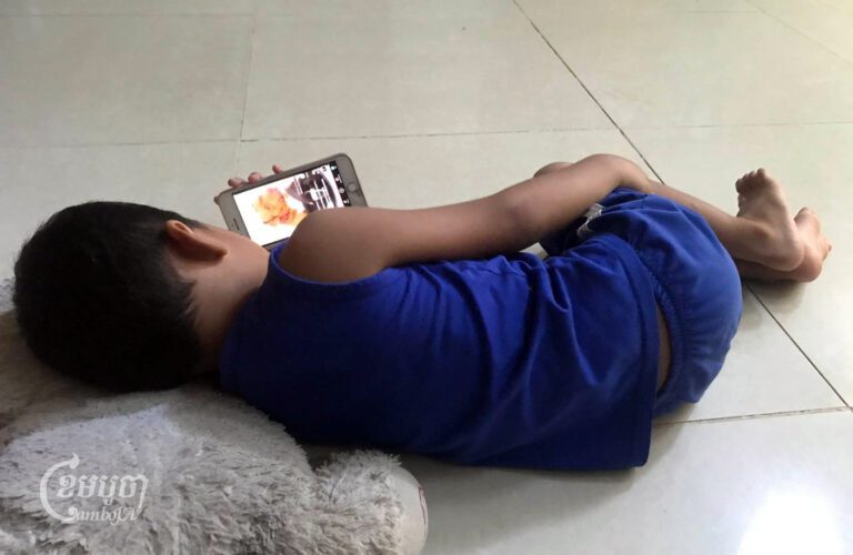 កុមារាម្នាក់កំពុងដេកមើលទូរសព្ទក្នុងផ្ទះ ស្ថិតនៅខណ្ឌដង្កោ រាជធានីភ្នំពេញ កាលពីថ្ងៃទី៣១ ខែឧសភា ឆ្នាំ២០២៤។ (ខេមបូចា/ គឹម សារុំ)