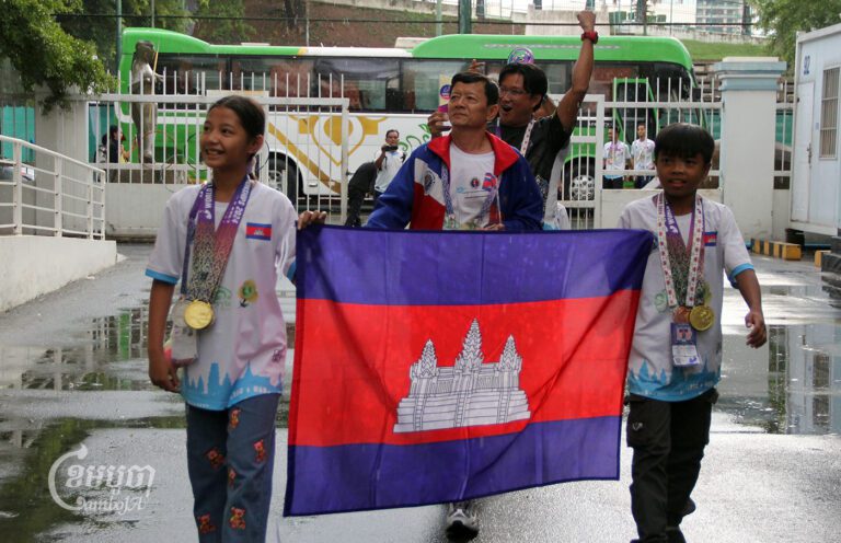 កីឡាការិនីវ័យក្មេង គង់ម៉ូណា ដាយអាណា ដែលឈ្នះបានមេដាយមាស២ ប្រាក់២ និងកីឡាករ សុខុន សីហនុត ឈ្នះបានមេដាយមាស៤ និងសំរឹទ្ធ១ ព្រមទាំងលោក គង់ ចាន់ធីណា និងគ្រូជំនួយ បានដើរដង្ហែទង់ជាតិកម្ពុជា ពេលជិះឡានក្រុងមកដល់ពហុកីឡដ្ឋានជាតិអូឡាំពិក នៅថ្ងៃទី៦ ខែសីហា ឆ្នាំ២០២៤។ (ខេមបូចា/ ស៊ា បញ្ញា)