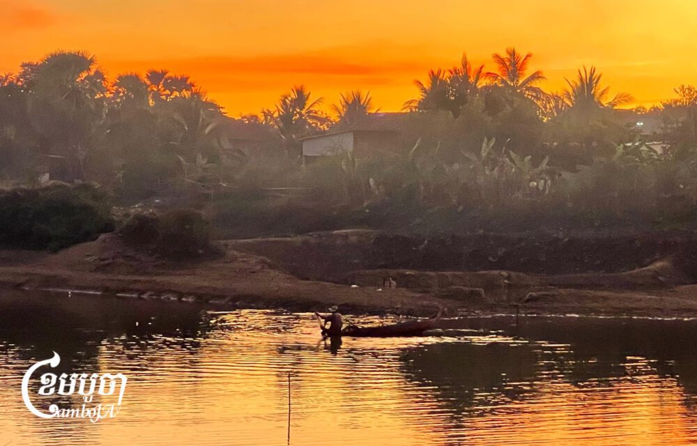 ទិដ្ឋភាពនៃអ្នកនេសាទម្នាក់កំពុងអុំទូកដោះត្រីមងនៅពេលល្ងាចក្នុងស្ទឹងស្វាយដូនកែវ ស្ថិតនៅភូមិស្វាយដូនកែវ២ ឃុំស្វាយដូនកែវ ស្រុកបាកាន ខេត្តពោធិ៍សាត់ ខណៈពេលដែលទឹកស្ទឹងបានស្រកស្ទើរអស់។ រូបភាពថតនៅថ្ងៃទី៣០ ខែធ្នូ ឆ្នាំ២០២៤។ (ខេមបូចា/ ឃី សុវុឌ្ឍី)