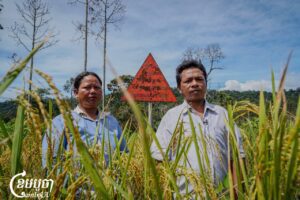 លោក ពក ង៉ែត និងភិរិយាឈរនៅខាងមុខផ្លាកសញ្ញាដែលព្រមានចំពោះអ្នកដុត ឬកាប់បំផ្លាញព្រៃឈើដោយខុសច្បាប់អាចប្រឈមនឹងជាប់ពន្ធនាគារពី៥ឆ្នាំ ទៅ ១០ឆ្នាំ។ រូបភាពថតកាលពីថ្ងៃទី២៩ ខែតុលា ឆ្នាំ២០២៤។ (ខេមបូចា)