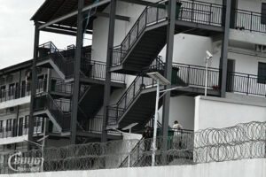 មនុស្សនៅក្នុងទីតាំងមួយនៅខេត្តតាកែវ នាថ្ងៃទី៤ ខែធ្នូ ឆ្នាំ២០២៤ ដោយមានសន្តិសុខយាមកាមយ៉ាងតឹងរឹង ដែលអាចមានទំនាក់ទំនងជាមួយទីតាំងមួយទៀតនៅជិតនោះដែលត្រូវបានសមត្ថកិច្ចបង្ក្រាបកាលពីខែតុលា បន្ទាប់ពីមានរបាយការណ៍អំពីការធ្វើទារុណ្ឌកម្ម។ (ខេមបូចា/ Coby Hobbs)