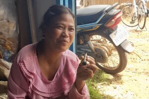 អ្នកស្រី សុខ មឿង ជាសមាជិកបណ្តាញសហគមន៍ប្រមេរុ កំពុងអង្គុយកាន់បារីមូដៃ ហើយផ្តល់បទសម្ភាសន៍ ដែលស្ថិតនៅឃុំប្រមេរុ នៃស្រុកត្បែងមានជ័យ ខេត្តព្រះវិហារ កាលពីថ្ងៃទី១៤ ខែមិថុនា ឆ្នាំ២០២៥។ (រូបភាព៖ លោក ម៉ម មុនីរតន៍)