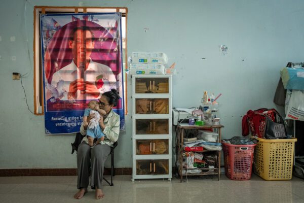 អ្នកស្រី យាន ស្រីយ៉ាន ភរិយារបស់លោក ស៊ុន ចន្ធី អតីតប្រធានគណបក្សកម្លាំងជាតិ (NPP) អង្គុយជាមួយកូនប្រុសអាយុ៤ខែ ឈ្មោះ ស៊ុន យានធាន ក្នុងបន្ទប់ជួលនៅក្រុងភ្នំពេញ កាលពីថ្ងៃទី២៤ ខែឧសភា ឆ្នាំ២០២៥ នៅមុខផ្ទាំងរូបភាពរបស់លោក ស៊ុន ចន្ធី ដែលចង់ភ្ជាប់ជញ្ជាំង។ (រូបភាព៖ រួន រី /HaRDstories)