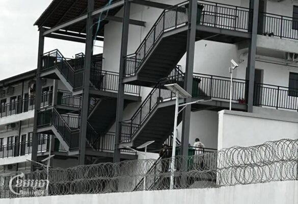 មនុស្សនៅក្នុងបរិវេណដែលហ៊ុំព័ទ្ធដោយរបងបន្លាលួសដឺរឹងមាំ ក្នុងខេត្តតាកែវ ដែលគេសង្ស័យថា មានទំនាក់ទំនងទៅនឹងទីតាំងមួយក្បែរនោះ ដែលត្រូវបាននគរបាលបង្រ្កាបកាលពីខែតុលា ក្រោយមានសេចក្តីរាយការណ៍អំពីការធ្វើទារុណកម្មនៅទីនោះ។ រូបថតថ្ងៃទី ៤ ខែធ្នូ ឆ្នាំ ២០២៤។ (ខេមបូចា/ Coby Hobbs)