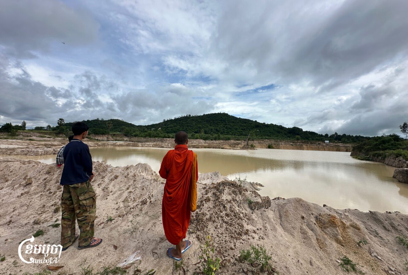 អ្នកភូមិ និងព្រះសង្ឃកំពង់ឈរសម្លឹងមើលទៅភ្នំពីមាត់រណ្តៅដី ក្រោយពីមានសកម្មភាពកាយយកដីលក់ កាលពីថ្ងៃទី២៩ ខែតុលា ២០២៥។ (ខេមបូចា/ ម៉ែន ចន្ធី)